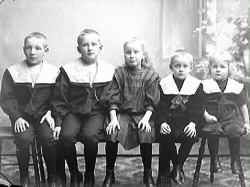 Barnporträtt. Fem syskon sitter på rad med en flicka i mitten. De fyra gossarna har alla mörka kortbyxkor och skjortor med vita kragar som når ända ut till axlarna och slips (sjömansliknande), flickan en rutig klänning.