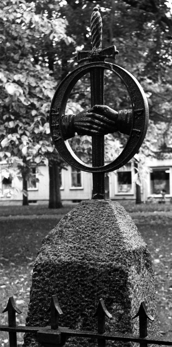 Närbild på Alströmers gravsten. Ett svärd med en cirkel runt bladet, från cirkelns mitt två händer som greppar svärdsbladet.