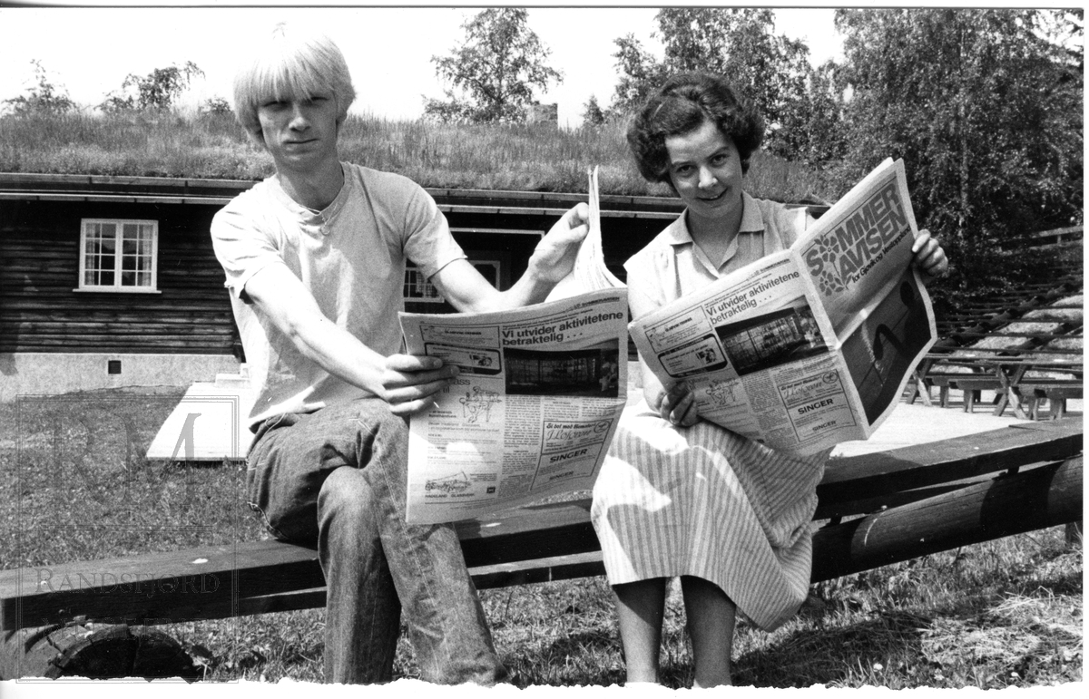 To personer sitter på en benk og leser i avis.