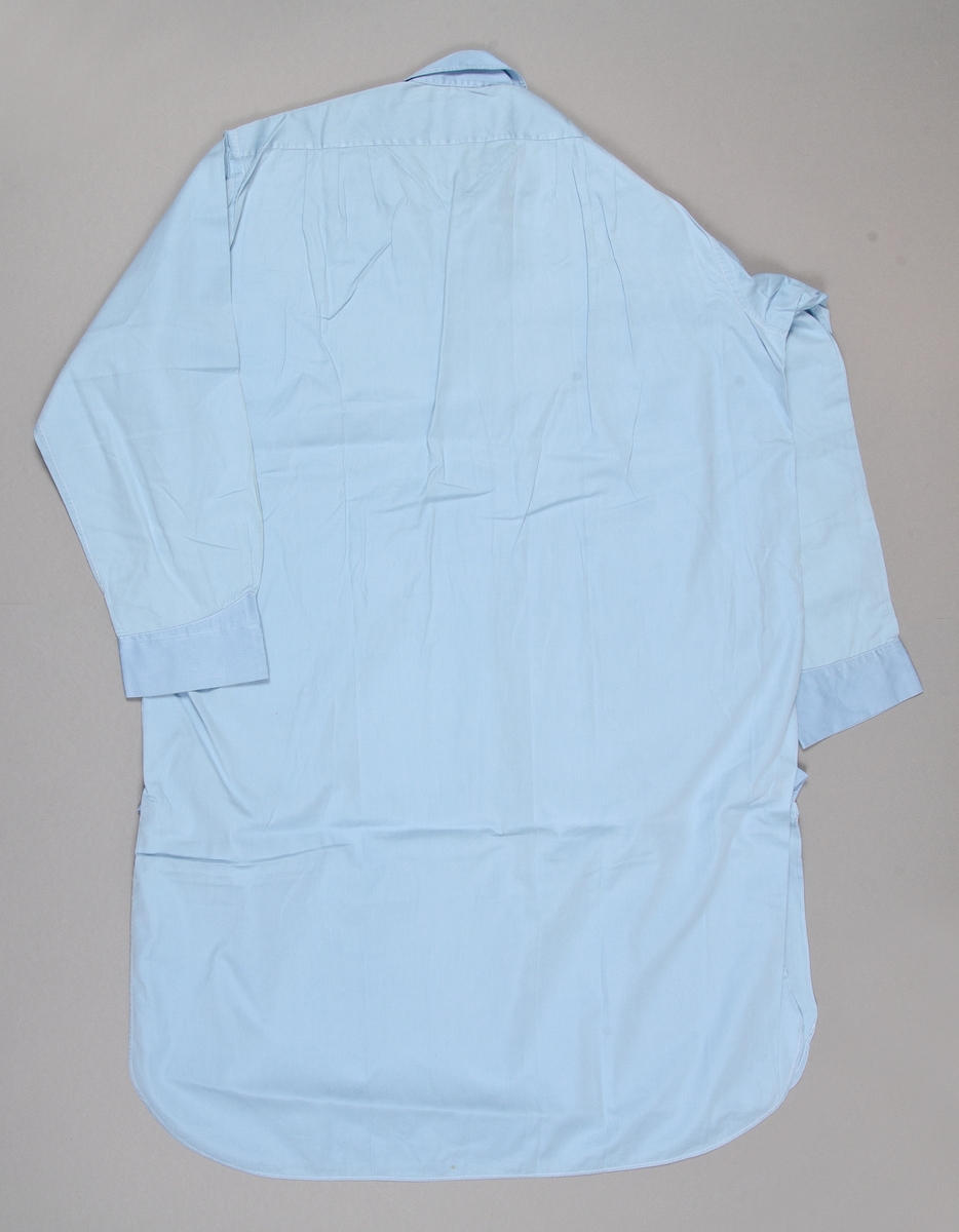 Nattskjorta av ljusblå bomullslärft. Krage. Långa ärmar. Sprund med knäppning framtill med tre vita knappar. Sprund i sidorna. Märkt med kedjestygn OJL framtill.
Stor reva på vänstra ärmen.