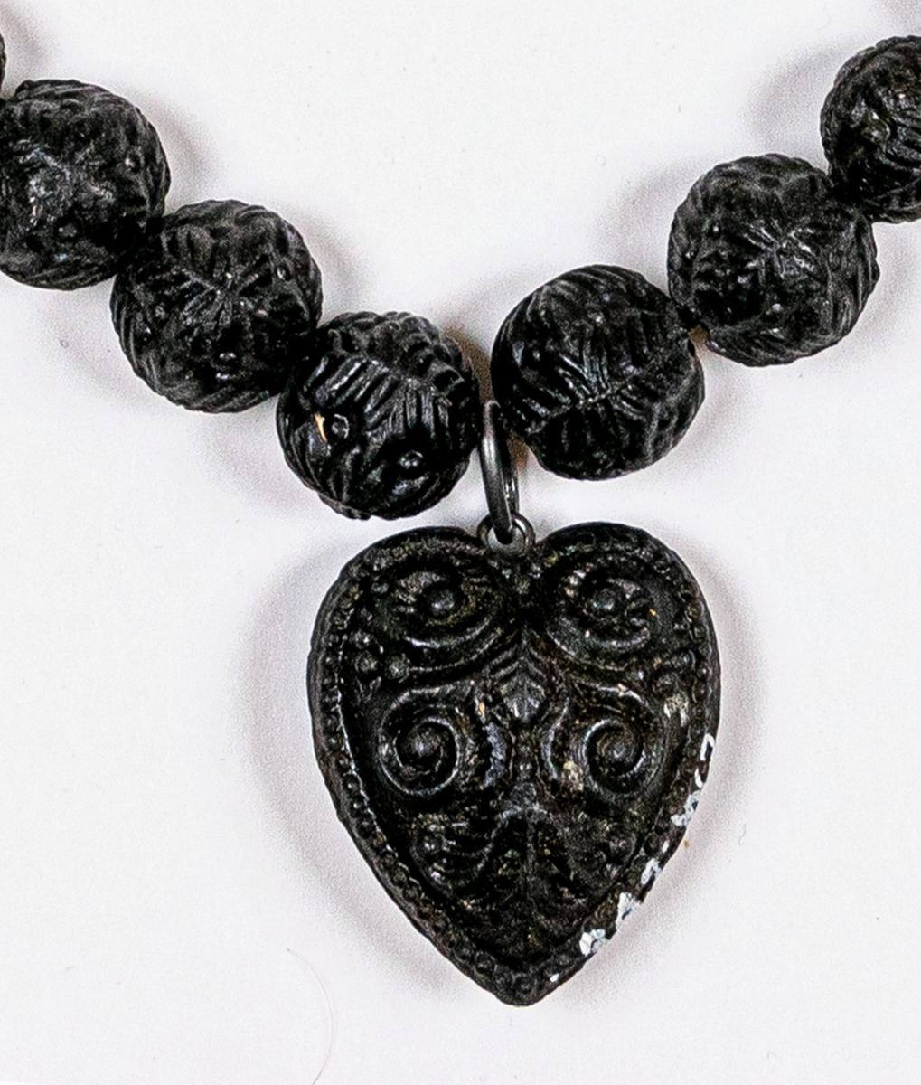 Halsband av svarta kulor, med ett hjärta som hänge. Stjärna och andra ornament pryder både hjärta och kulor. En del kulor saknas. Sannolikt gjuten konstmassa som guttaperka.