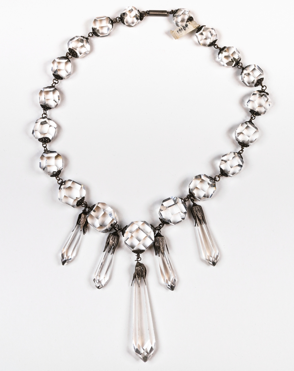 Halsband, av stora slipade glaspärlor, samt en större och fyra mindre droppformiga hängen. Pärlorna äro 19 st.