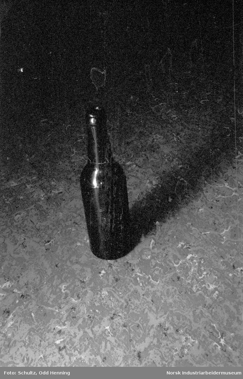 Flaske i farget glass som står på gulvet.