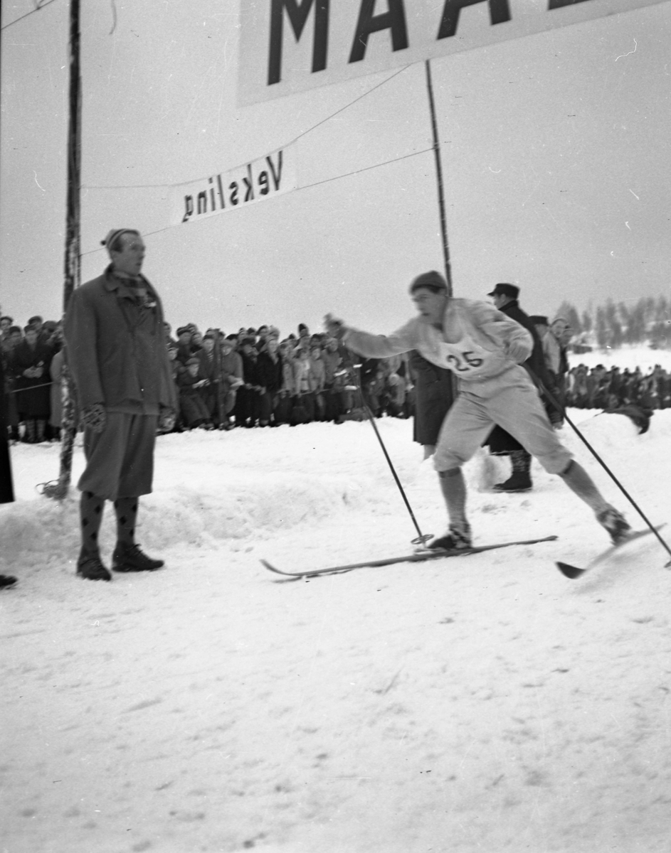 En skiløper med startnummer tjuefem i full fart i løypa. Mange tilskuere sees i bakgrunnen.