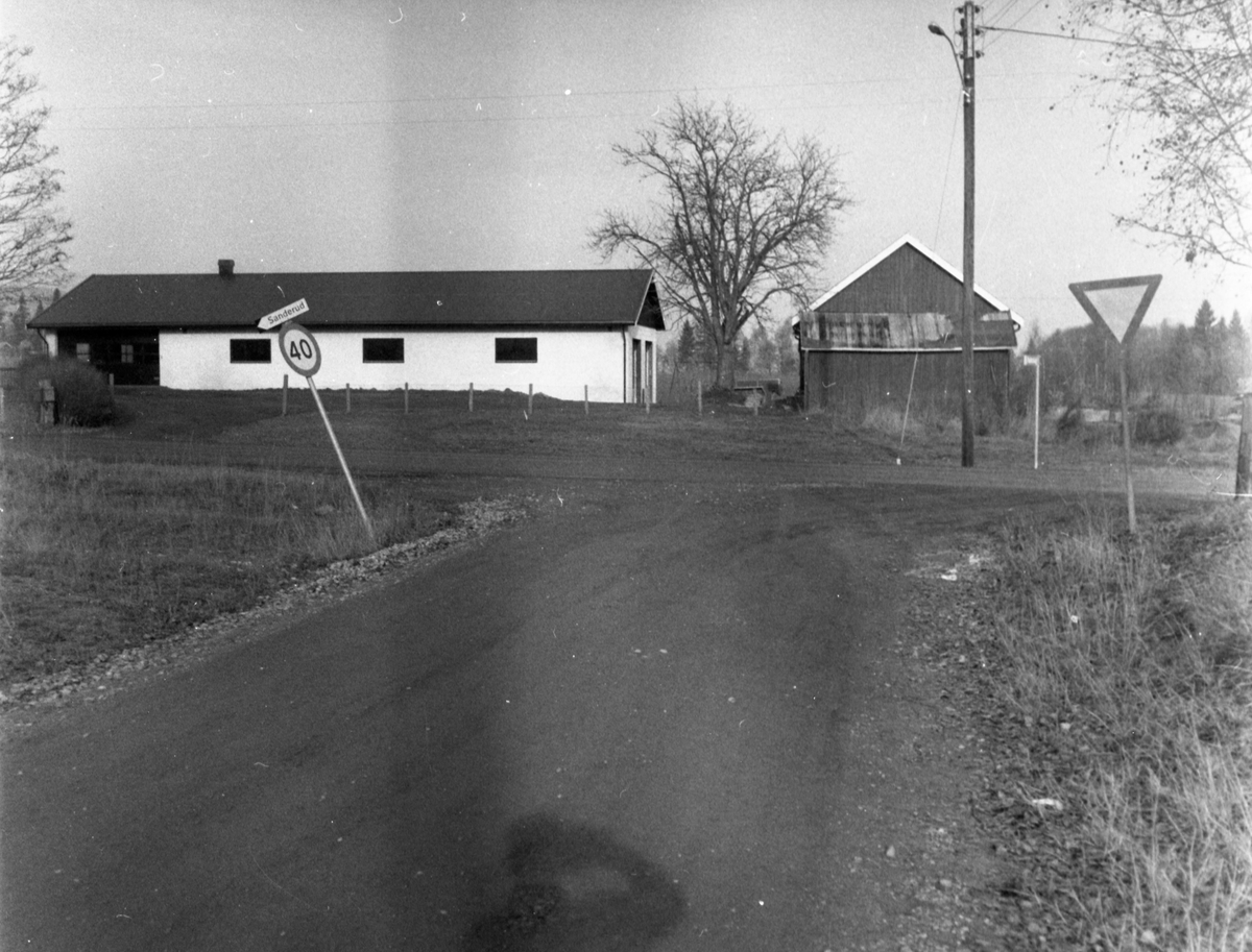 Et veikryss med bygninger, et 40-skilt og vikeplikt-skilt. Sanderud er skiltet til venstre.