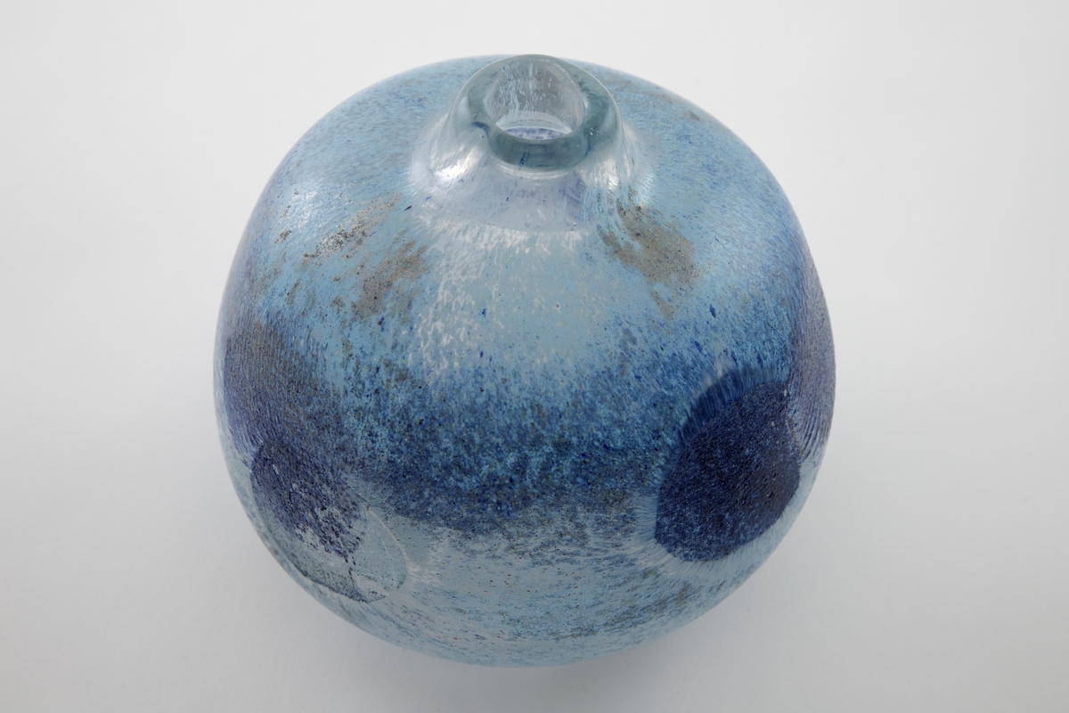 Kuleformet vase med kort hals og liten munning. Klart glass med innlagte metalltråder samt -netting, hvor overflaten er dekorert med blå-, brun- og grønnspettede partier.
