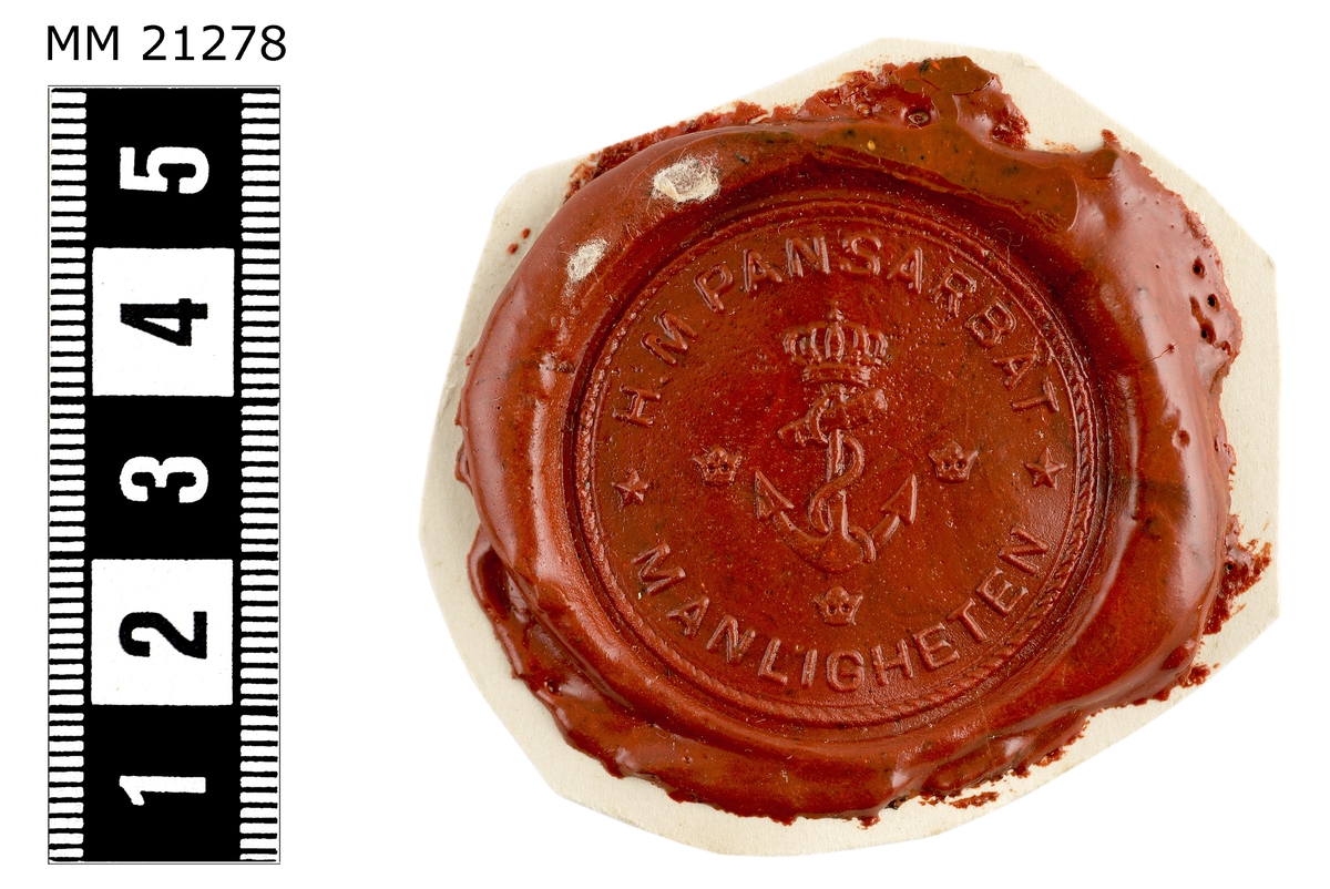 Sigillavtryck av rött lack på papper. I mitten krönt stockankare omgivet av tre kronor. Längs kanten text: "H.M. Pansarbåt Manligheten".
