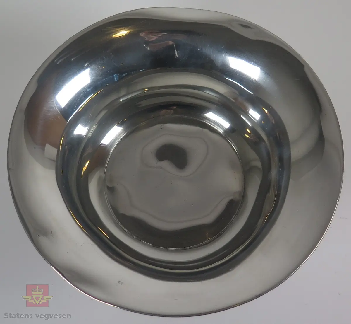 Pokal i sølv formet som en skål/bolle. Det er utformet tre ørner mellom bunnen og toppen av pokalen.