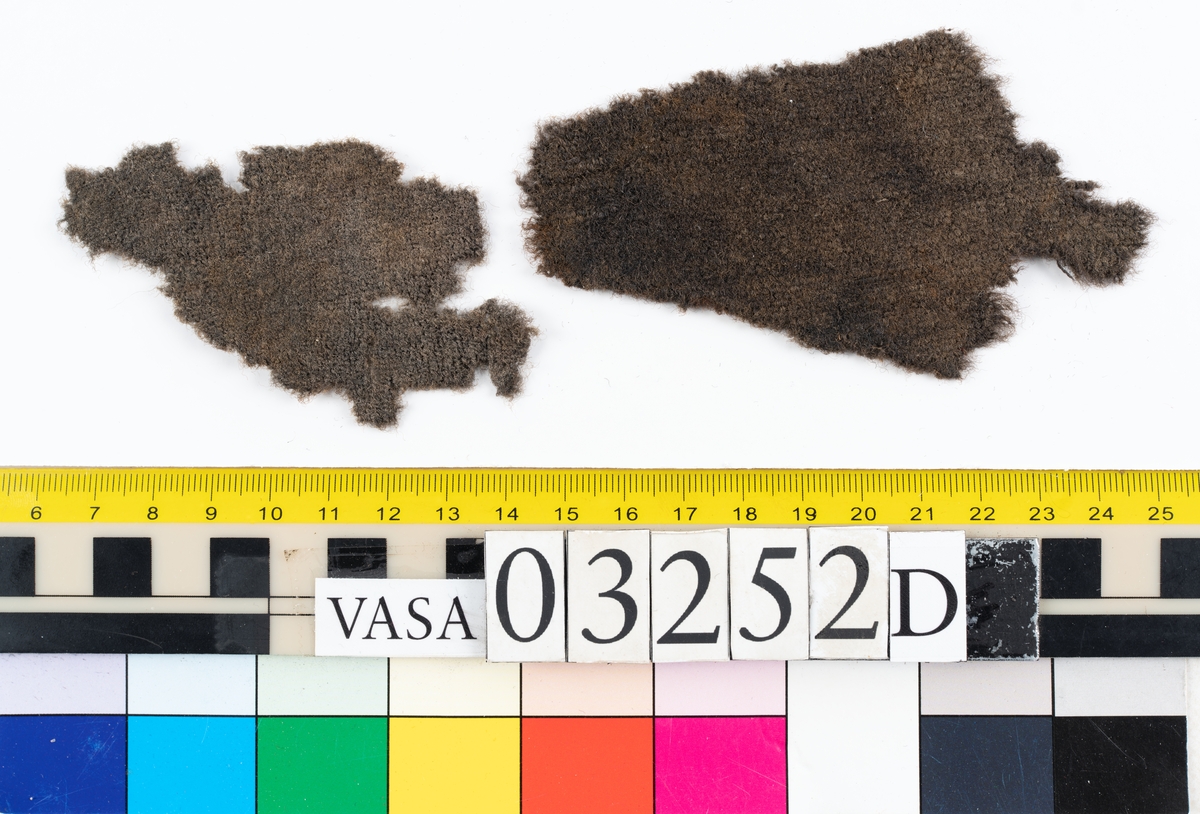 Textilier. 
14 textilfragment uppdelade på fyndnummer 03252a-d.
Fnr 03252a är ett silkesband. 
Fnr 03252b är ett textilfragment av ull vävt i tuskaft. 
Fnr 03252c består av 10 fragment av ull vävda i tuskaft. Flera av fragmenten har bevarade originalkanter med sömmar.
Fnr 03252d består av två fragment av ull vävda i tuskaft.