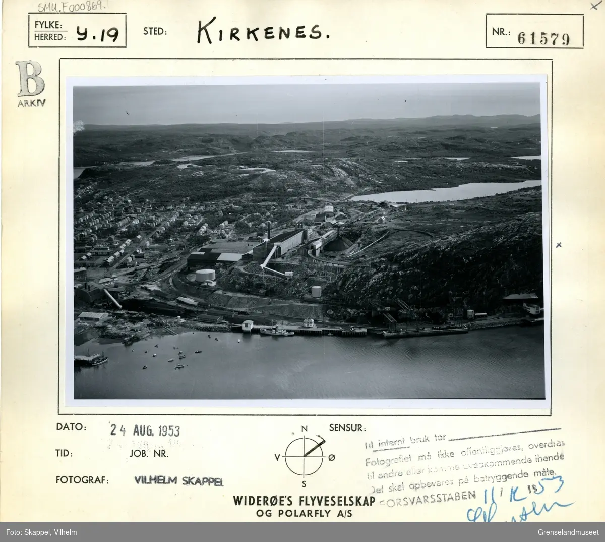 Flyfoto av AS Sydvaranger anlegg i Kirkenes sentrum. Deler av bybebyggelsen sees til venstre i bildet. Lokstallen ligger midt i bildet med Førstevann rett ovenfor og mot høyre. Kaianlegget i front.
