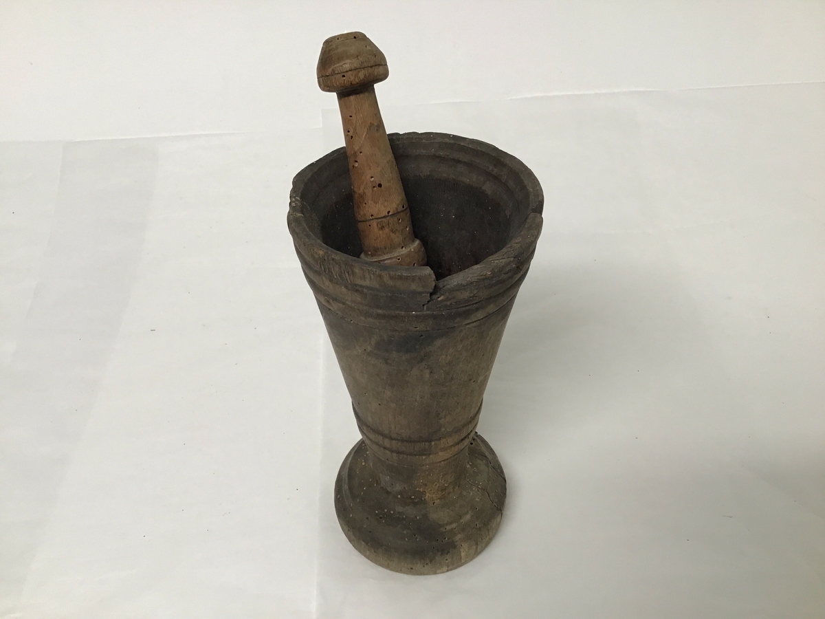 Både mortar og pistill er laga av tre, mortar er sylinderforma svakt kon  med stett. Mortaren har ein skade øvst i munning.