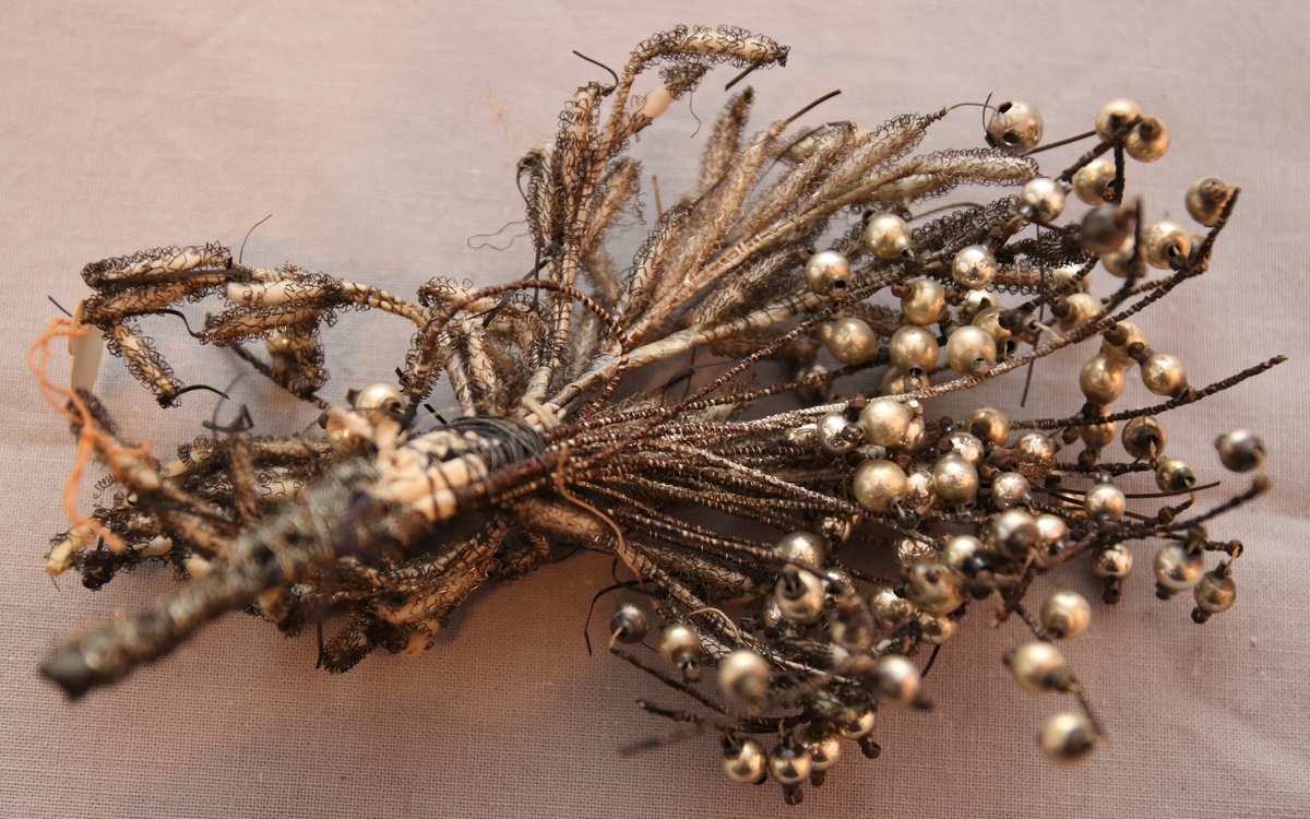 Hårprynad i form av ett knippe/bukett utformat av tråd, textil och med hängande silverpärlor.