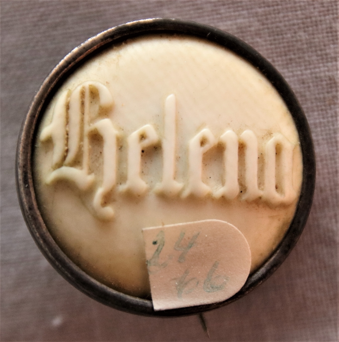 Brosch ägjord av ben, möjligtvis elfenben. Med namnet Helena utskuret i relief på framsidan. Broschen är inramad av en silverkant och stämplad: B.E.  ?  N. 7?
