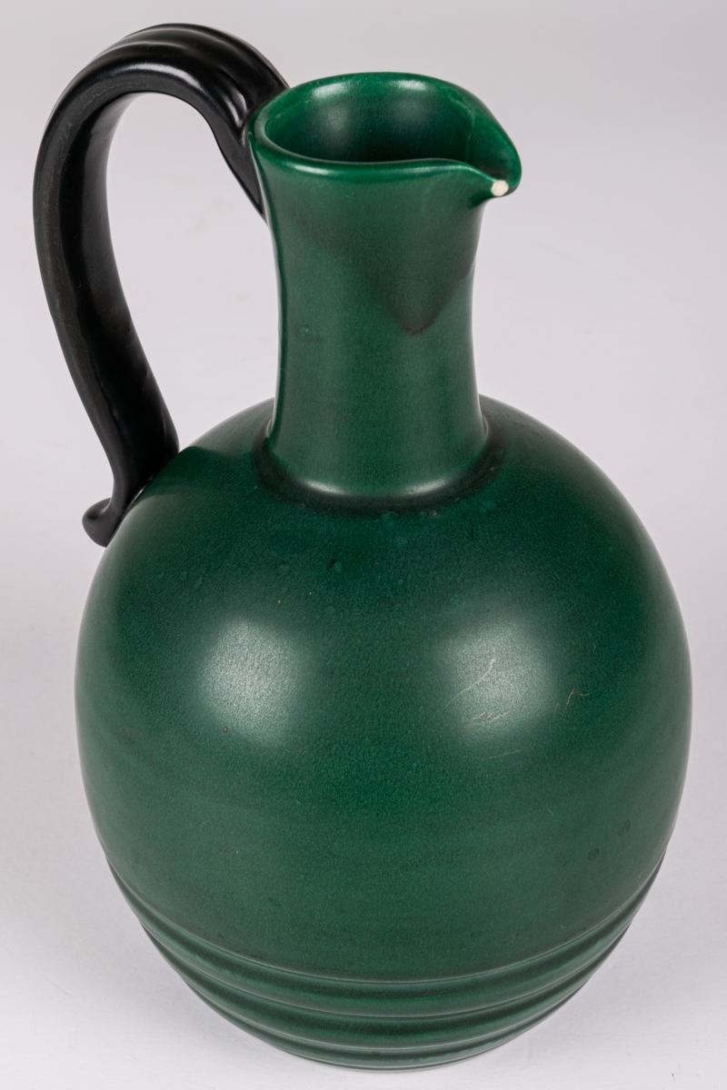 Likörkrus med pip och hänkel, lergods, modell 4346 av Eva Jancke-Björk, formgiven 1934. Glasyr MK, svartgrön matt glasyr som användes åren 1934-1937.