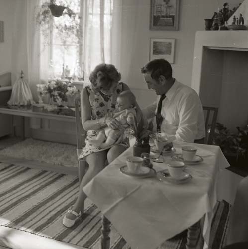 Lill-Annas dop sommaren 1973, här i ett rum på gården Sunnanåker. En man och en kvinna sitter med dopbarnet i knät vid ett dukat kaffebord.