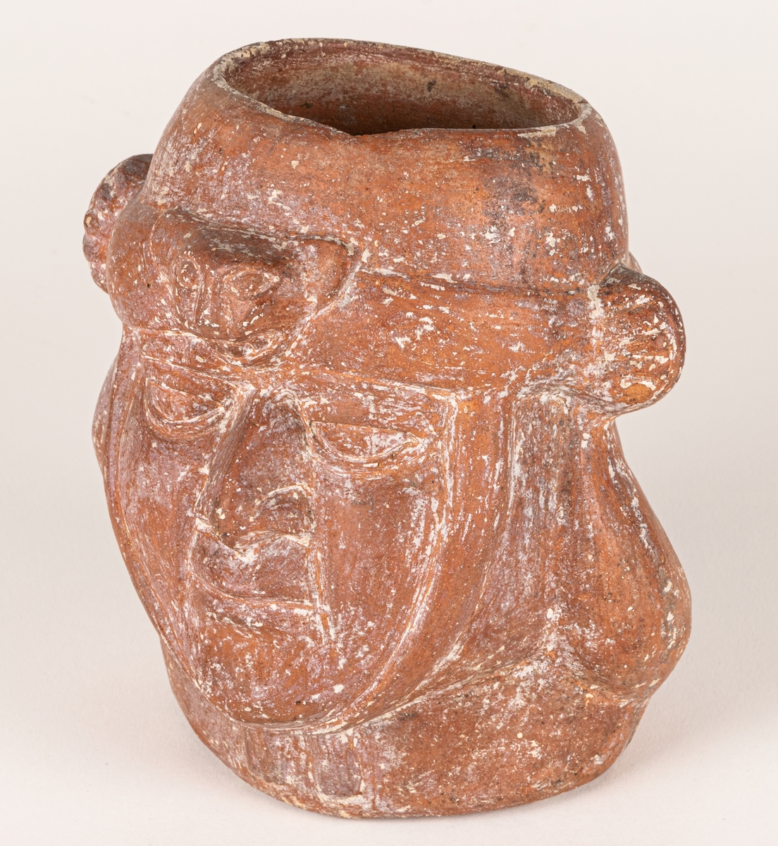 Gravkärl, av rödbrun lera med kraftig relief i form av ett ansikte. Ova öppning upptil. Inkaiskt gravkärl.