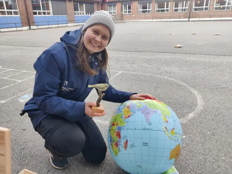 Foto av naturveileder i en skolegård med trefugler og en globus