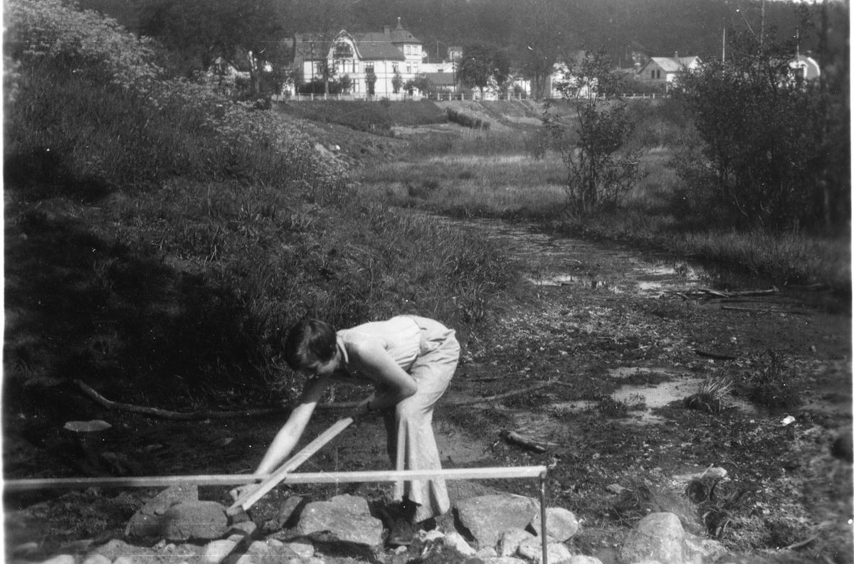 Fröken Ingegerd Sjöberg mäter stenar i en stenpackning i den miellersta vallgraven (grav II) vid Rumlaborg i Huskvarna. Fotot är taget i samband med arkeologiska undersökningar sommaren 1932.