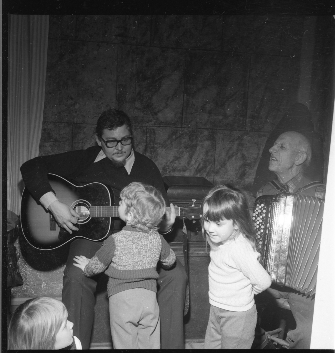 Barn står framför två män som spelar gitarr respektive dragspel. Det är Ölmstad hembygdsförenings julfest.