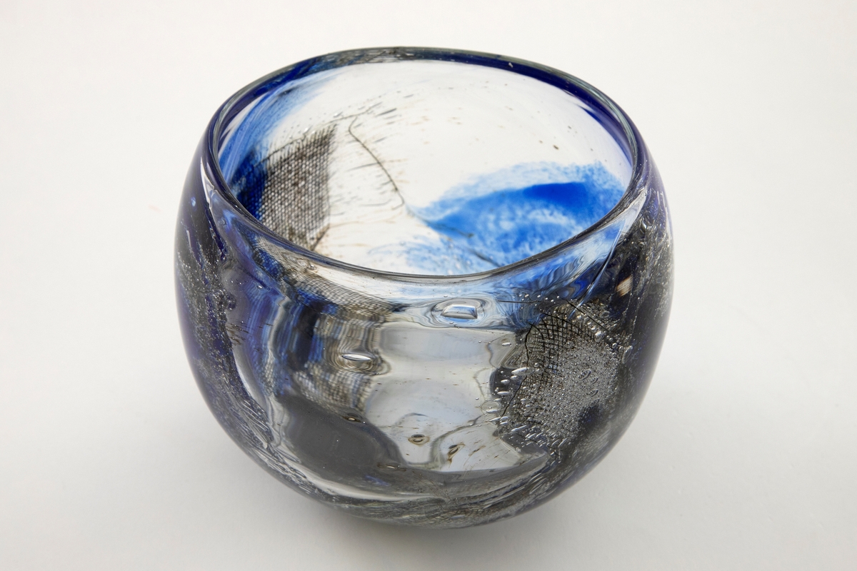 Bolle i klart glass med ovalformet munningsrand. Dekor av innlagt metallnett, blå farge og luftbobler