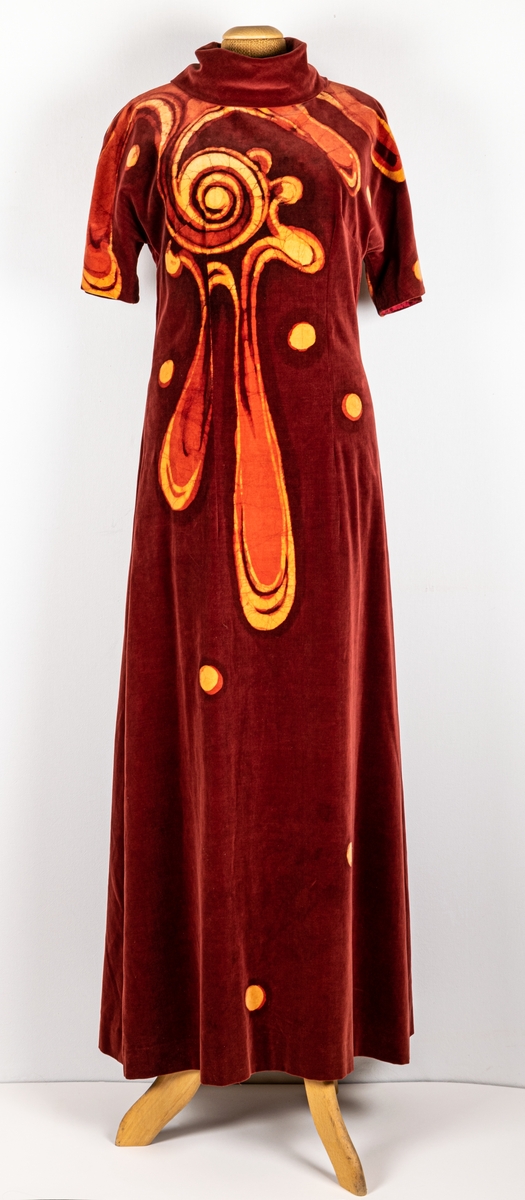 Långklänning i mörkröd sammet i batik. Dragkedja i rygg och hög krage. Klänningen är signerad EL i batik.
