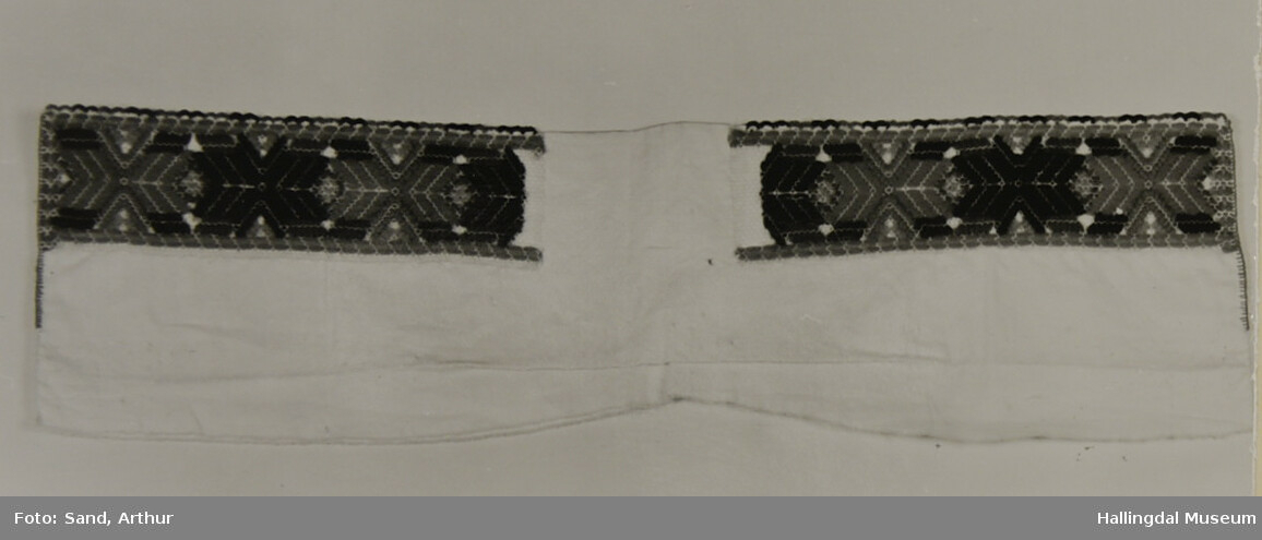 Halskrage brodert med ullgarn på tyll og sydd fast på bomullslerret, 4 cm breit. 6,8 cm bak er ikke brodert. Tungekant øverst.