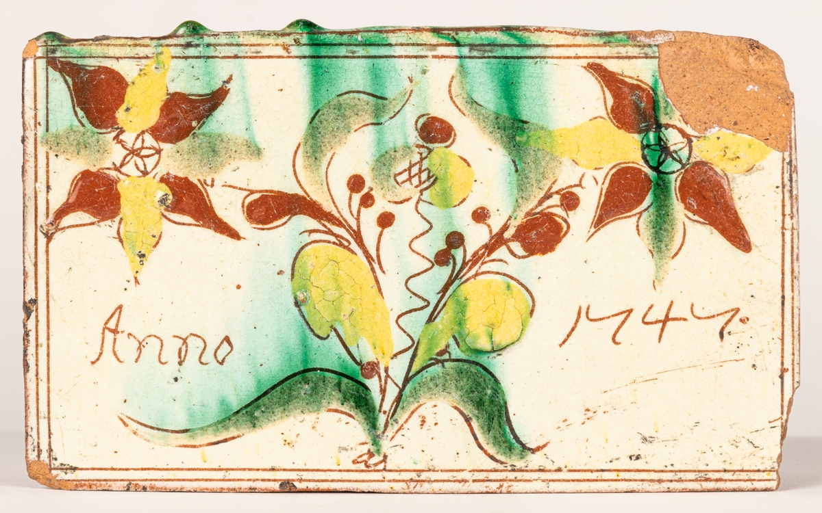 Kakel och lergods.
d, glaserade, vit botten med blomster m.m. i gul-brun-grön färg. 1700-tals kakel.  Totalt 14 stycken. Blomtermotiv m.m. ett fragment av flicka bärande två vattenämbar. Några daterade mellan 1744 och 1748.