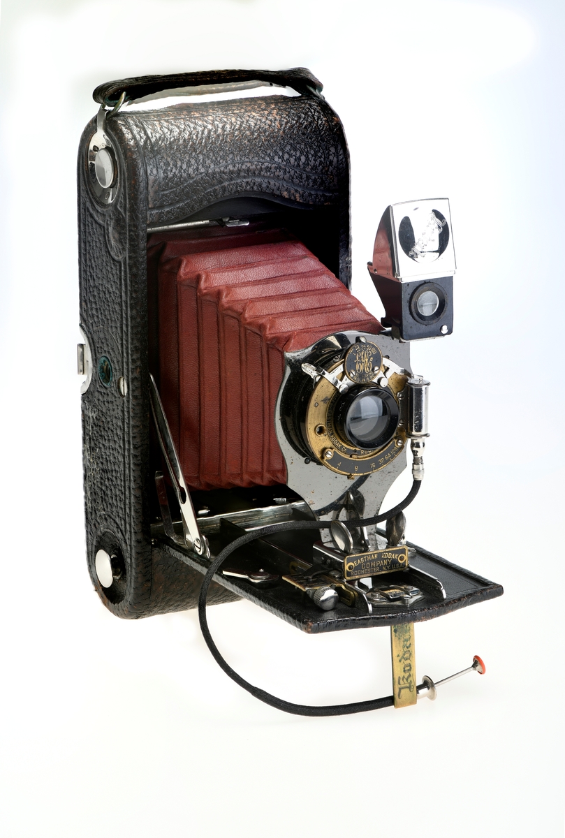 Et belgkamera for 116-film fra Kodak. No. 1A Folding pocket ble laget i flere versjoner mellom 1899 og 1915 og var det første kameraet fra Kodak til å bruke 116-film. Av de fire versjonene (Model A, B, C, D) var denne Model D den første til å ha en objektivplate i metall, mens de tidligere versjonene hadde en objektivplate i tre. 

Kameraet tar bilder på 6,5x11 cm. Det har 3 lukkertider i tillegg til åpen lukker (B). I tillegg til lukkeren på objektivet har kameraet også en snorutløser. På skinnen som belgen er festet i er det et lite hjul for å stoppe belgen i ulike posisjoner merket med fokusavstand. Det er en søker foran på objektivplaten som kan roteres for å ta landskapsbilder, og søkeren har et deksel som kan vippes opp. Baksiden kan åpnes for å sette inn film, og det har et rødt vindu for å se om det er film i. Luken til belgen åpnes med en knapp på siden av kameraet, på luken er det en fot som kan brettes ut. Håndtak i skinn på toppen. Kameraet kommer i en veske av skinn. Med kameraet følger også en mekanisk opptrekkbar selvutløser som kan festes på enden av snorutløseren.
