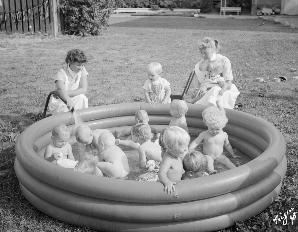 Fotografi av barn som leker i badebasseng og ansatte på Aline spebarnshjem.