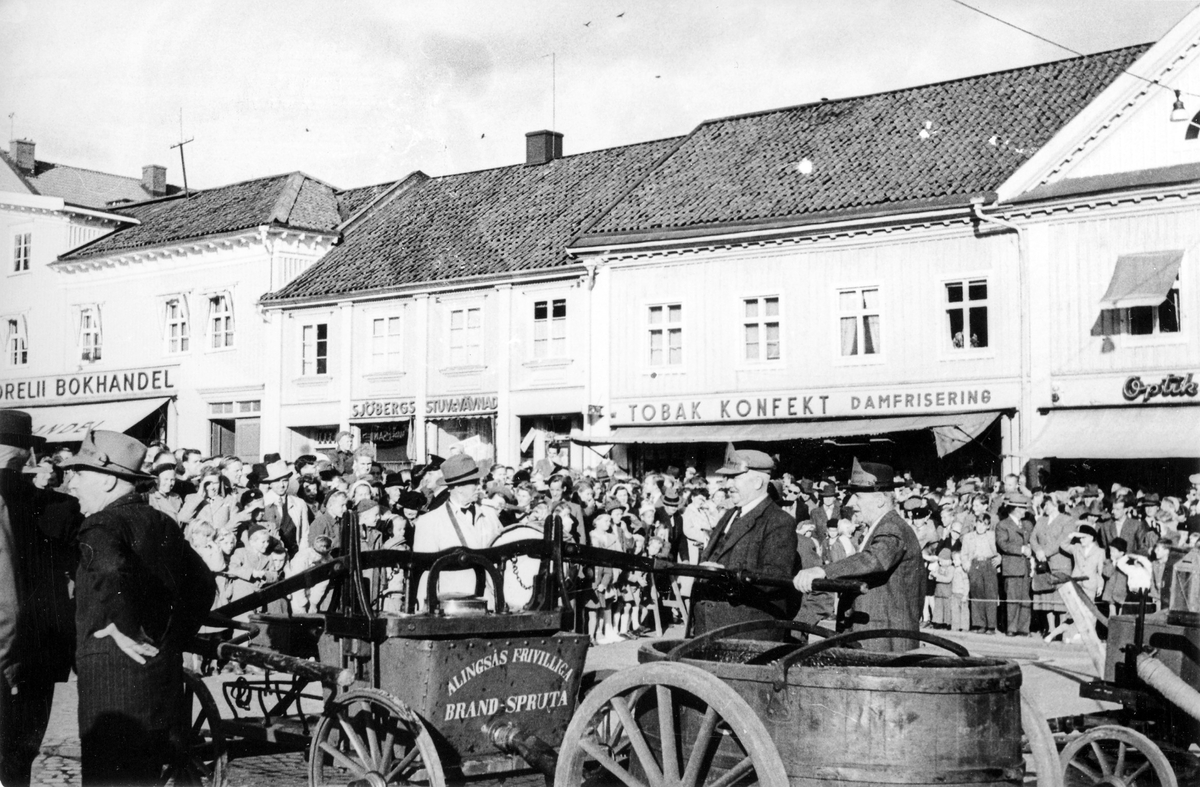 Brandkårens 50-års jubileum 1950. Gamla brandredskap demonstreras på Stora torget av några män inför en folksamling.