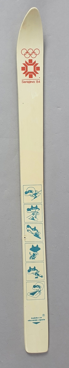 Hvit miniatyrski med emblemet til de olympiske vinterleker i Sarajevo i 1984. Det er motiv av maskoten for lekene, ulven Vuchko, som utøver ulike idretter. 