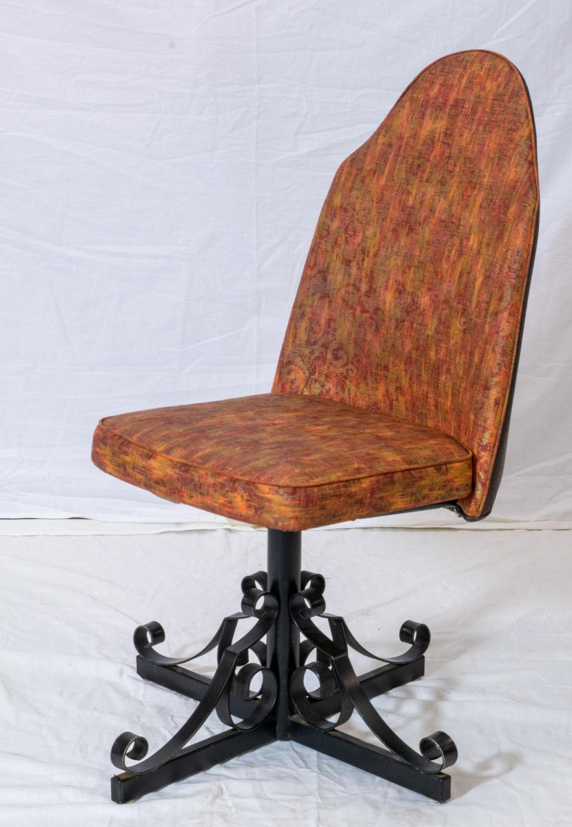 Spisestuestol med rødbrunt trekk. Bein i sort metall minner om smijern og bakplate i plast med tremønster. Stolen kan snurre.
