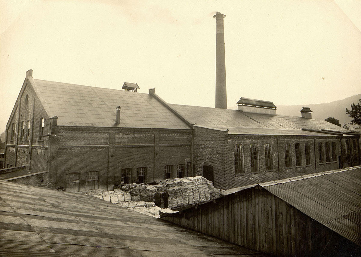 Sort-hvitt bilde av en fabrikkbygning i murstein med en skorstein