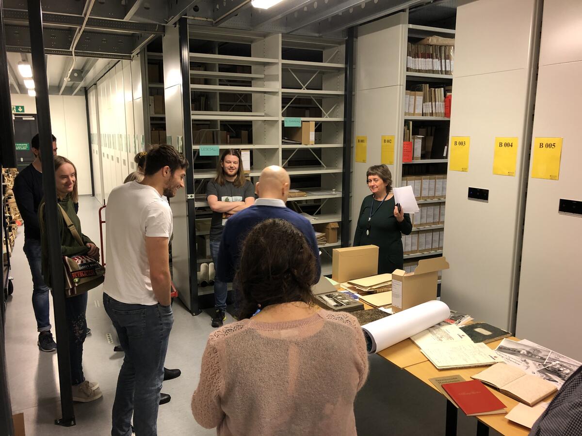 En gruppe mennesker står inne i arkivet. Foran dem er det et bord med papirer og mapper.