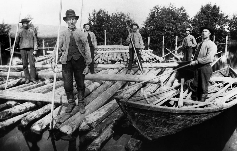 Gammelt foto av fløtere med tømmer og robåt.