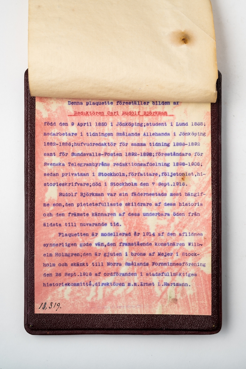 Plakett i brons, monterad på träplatta klädd med tunnt skinn, med bild av redaktör Rudolf Björkman i profil. På baksidan är ett maskinskrivet papper fastsatt med text om Rudolf Björkman.