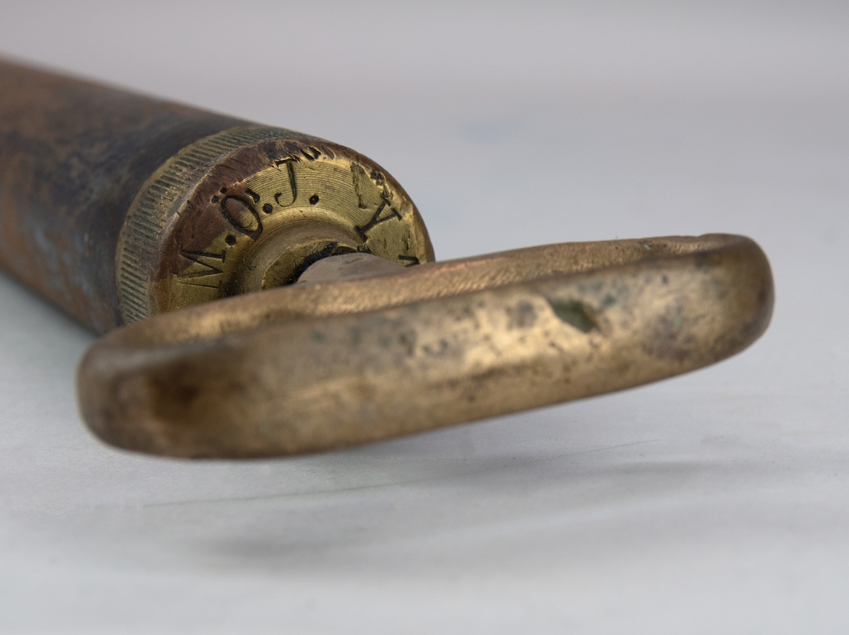 Oljespruta av metall, cylinderformad med avsmalnad, krökt pip. Rester av svart färg. Ovalt handtag sitter fast i locket. På locket står det "M.Ö.J. Y 11".