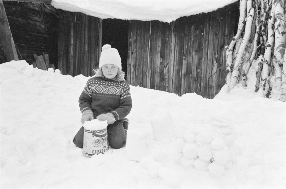 Et barn leker i snøen med en bøtte.