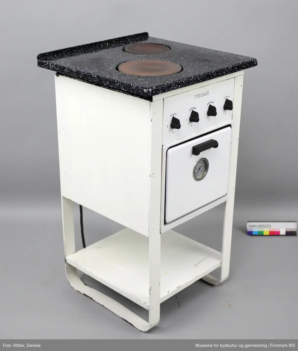 Den elektriske komfyren "Vegar K2" har to kokeplater, en stekeovn og en hylleplate nederst. Fram- og bakben er utformet som buer på hver side. Apparatet har fire vrideknapper, en for hver plate, samt for over- og undervarme i ovnen. På ovnsdøra er det et rundt termometer som viser temperaturen i ovnen. I ovnen er det to lave og et dypt stekebrett, samt en rist. Typeskiltet befinner seg på baksida. Strømkabelen er svært porøs og mye av isoleringen har falt av.