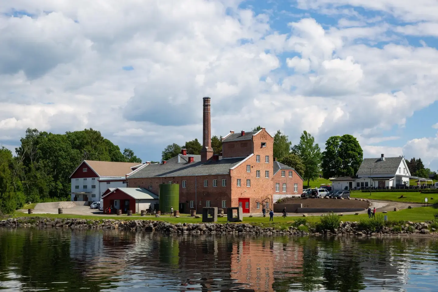 Atlungstad brenneri sett fra ei brygge. Brenneriet speiler seg i vannet og det er sommer.