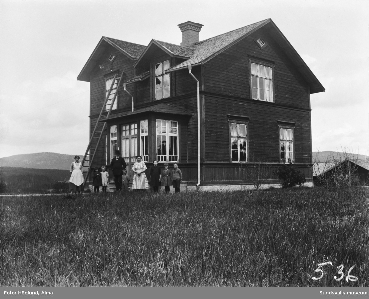Två bilder på en familj framför glasverandan till sin bostad. En man, två kvinnor och sex barn. Andra bilden, en närbild på familjen.