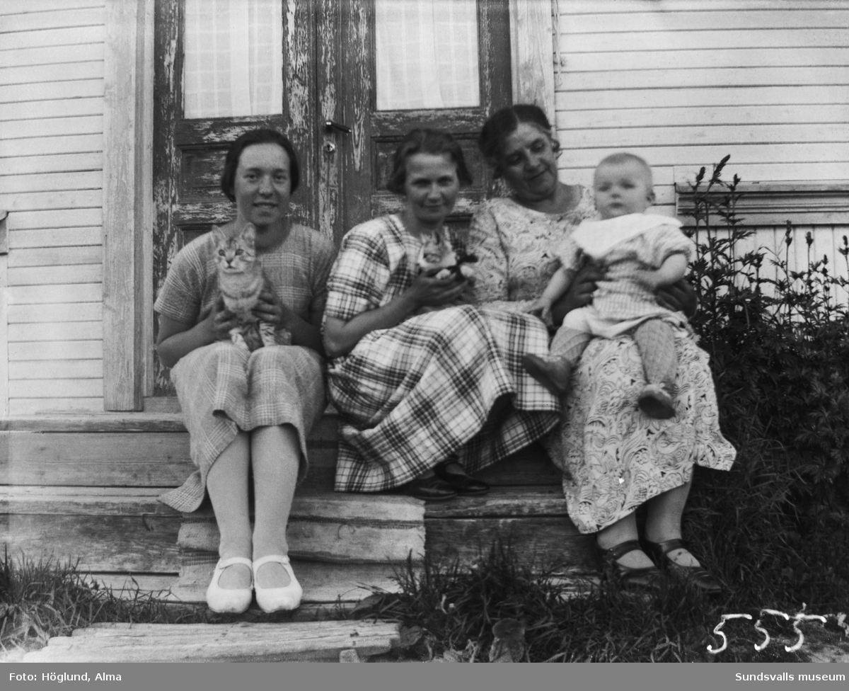 Hilma Höglund samt två kvinnor, en baby och två katter sitter på trappen till ett hus.