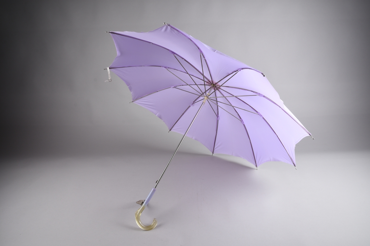 Paraply med 10 spiler og stang i metall. Handtak i plast, tofarga, lilla og gulkvit gjennomsiktig. Hempe i tekstil for å ha handa i. Lys lilla duk i kunstfiber.