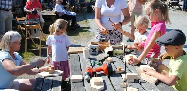 Barn som lager plankebåter rundt et bord, ute, sol.
