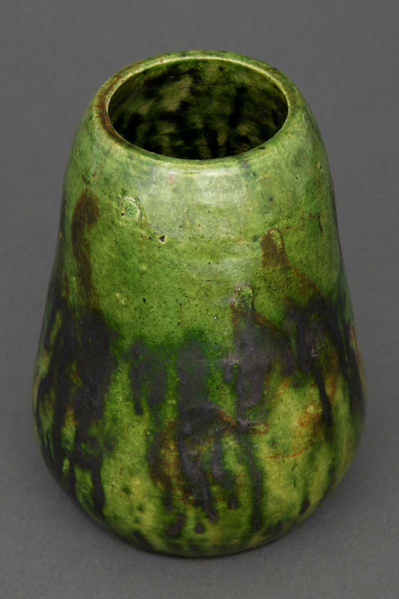 Liten vase i dreid leirgods. Vasen har pæreform og er glasert med grønn flyteglasur og rennende svart jernglasur.