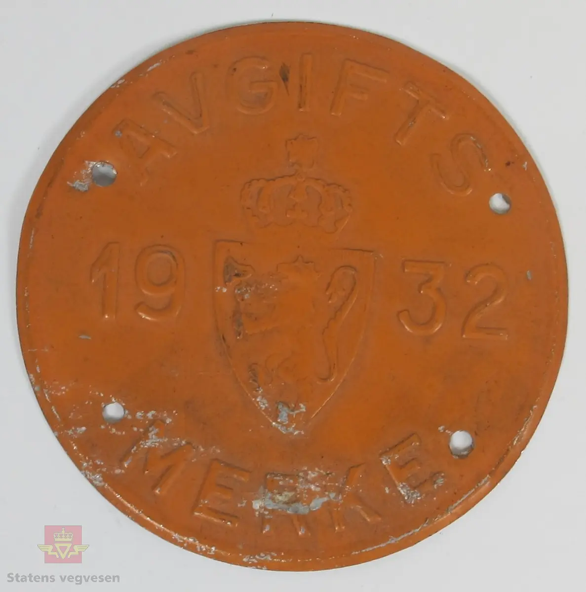 Rundt avgiftsmerke i oransje med utstanset skrift og det norske riksvåpenet. Merket har teksten: AVGIFTS MERKE 1932.