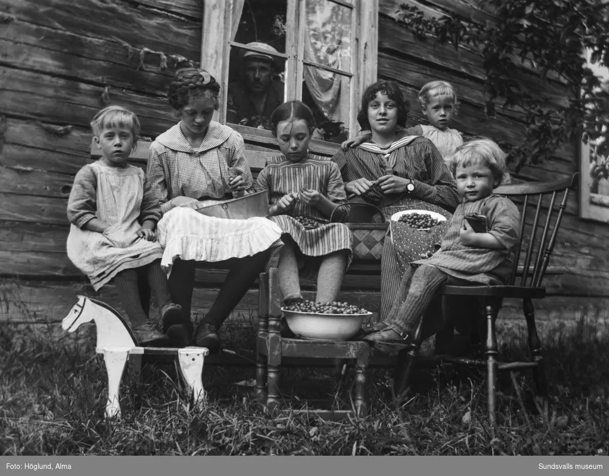 Barnen Höglund och två andra flickor rensar krusbär utanför bostaden i Fanbyn. Från vänster: Ingrid, oidentifierad, Hilma, Elin Dalenius, Irma och Per. I fönstret syns Gottfrid Höglund.