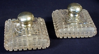 :1-2 Två likadana flaskor av genomskinligt glas, låga, kvadratiskt formade. På utsidan ett rutformigt mönster i ytan. Öppningen igenpluggad av en kork av glas, ovanpå vilken en silverhatt skruvas fast som kork.