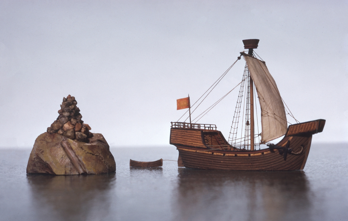 Fartygsmodell, vattenlinjemodell, hel i block av trä, kogg (1400-talet). Brunt skrov med höga kastell i för och akter Riggad med 1 mast med ett råsegel, rund stridsmärs. På akterkastellet stång med röd flagga med heraldiskt vapen. Utrustad med skeppsbåt.Föremålets form: Vattenlinjemodell