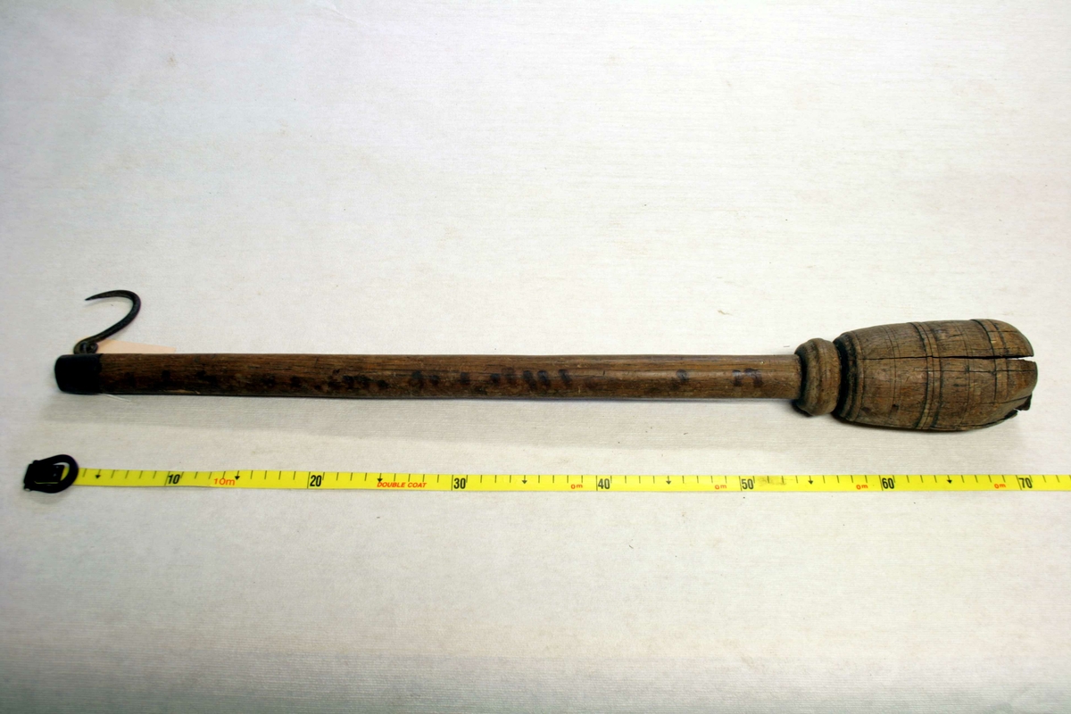 Kluppeformet mortel-stang, med jernbolt i midten festet med bly, kort treskaft med liten og spiss jernkrok øverst på skaftet